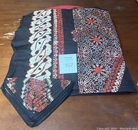 Folded Indonesian Batik tablecloth with six matching batik napkins placed on a wooden surface. The batik fabric shows traditional floral and geometric patterns with black, red, and beige coloring.