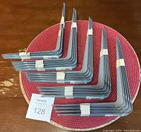 Eighteen grey metal shelf brackets laid out on a circular red placemat on a wooden surface, showing the size and design clearly.