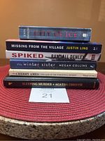 Stack of six books on a red placemat, titles visible on spine: City of Ice, Missing from the Village, Spiked, The Winter Sister, The Case of the Forgetful Patient, Sleeping Murder.
