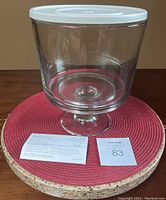 Glass trifle bowl with plastic lid fitted on top, sitting on round textured cork mat.