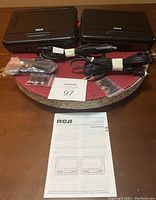 Two RCA portable DVD players with cables, headphone adapters, and instruction manual laid out on a table.