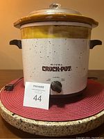 Front view of the Rival Crock-Pot slow cooker showing control knob, handles, and glass lid on a red surface.