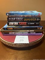 Stacked books show variety of sci-fi and comic related titles including Star Trek, Amulet, Minecraft, Wonder Woman, Analog Magazine, and Alien Landscapes.