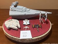 Photo showing six Star Wars toy vehicles displayed on a round red mat, including a large grey Imperial Destroyer, Millennium Falcon, BB-8 droid, TIE Fighter, X-wing, and small starfighter.