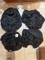 Four black tire storage and carrying bags laid out on tile floor, showing circular shape and opening closures.