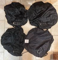 Image showing four round black tire storage bags with drawstrings and buckled straps on a tiled floor.