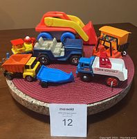 Photo showing six vintage toy vehicles on a round stone tray with a woven red mat under them, displaying various colors and types.