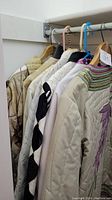Side view of six beige handmade jackets hanging on a rack showing various stitched patterns and textures.