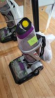 Full view of Bissell Revolution carpet cleaner showing purple details, black wheels, power cord wrapped in a bag, and clear tanks on wood floor.