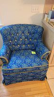 Front view of blue floral side chair showing button-tufted backrest, padded armrests with fringe trim, and pleated skirt.