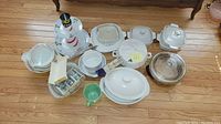Overview of CorningWare dishes including casserole dishes, glass lids, and other ceramic items arranged on wood floor.