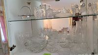 Glass cabinet displaying an assortment of cut glass bowls, plates, glasses, decanter, and other glassware.