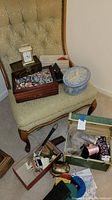 Photo shows multiple decorative boxes including wooden and fabric-covered blue hatbox, a small clock, and several small items such as sewing thread spools and jewelry scattered around and inside boxes.