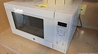 Front and side view of white GE microwave on counter, showing digital clock and control panel