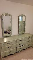 Front view of the green dresser with nine drawers and two matching green framed wall mirrors above it.