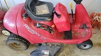Full side view of red Honda Harmony 1011 riding lawnmower showing seat, control levers, and side discharge chute.