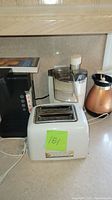 Photo shows a white two-slot toaster, white food processor, and copper electric kettle on a kitchen counter.
