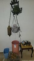 Photo showing all items in the lot including lantern, hanging planter, three plastic planters, metal log holder with pinecones on the floor, and wooden side table with items on top.