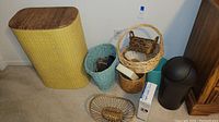 Yellow woven laundry bin, blue basket, smaller baskets, black trash bin, and box on carpet near outlet