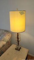 Full view of MCM style cut glass lamp on a side table, glowing warm light from drum shade