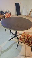 Round dark woodgrain tabletop with black metal base and one floral upholstered chair visible