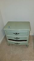 Front view of the painted green night stand showing three drawers with metal handles and signs of wear.