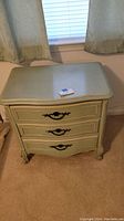 Front and top view of the green painted night stand showing three drawers with black metal handles and worn surface.