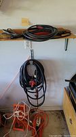 Photo showing coiled thick black power cord with red connectors and multiple black cords on shelf, plus orange and white extension cords on floor