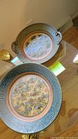 Two glaze textured ceramic plates on glass table, larger 16 inch with loop handles, smaller 13 inch plate.