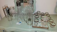 Multiple glass carafes and glasses with silver rims, arranged on a green desk with a mirror in the background.