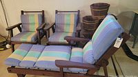 Side view showing wooden lounger with blue, green and yellow striped cushions and two wooden armchairs with matching cushions.