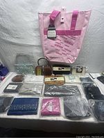 Full lot displayed against white fabric backdrop, includes pink Adidas tote bag, various clutches and wallets in different colors and styles, some with tags and in packaging.