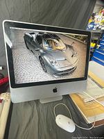 Front view of Apple iMac desktop computer powered on displaying a high-resolution image, situated on a surface with a wired Apple mouse to the side.