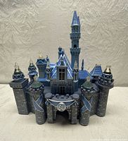 Front view of the Sleeping Beauty Castle model showing the entrance, towers, blue roofs and 60th anniversary emblem.