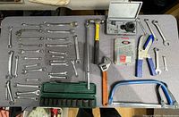 Full view of the lot showing combination wrenches, adjustable wrench, hammer, hacksaw, rivet gun, socket set, and drill bit sets, laid out on a table.