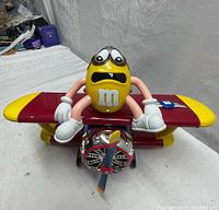 Front view of the large yellow M&M character candy dispenser sitting on a red and yellow bi-plane with chrome propeller.