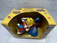 Front and side view of boxed vintage M&M's jumbo jet airplane chocolate dispenser with yellow M&M figure inside.