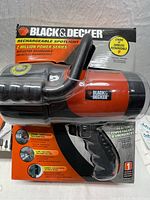 Front view of Black & Decker rechargeable spotlight in original packaging showing large reflector. Orange and black design.
