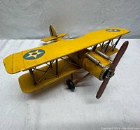 Front-side angle of yellow metal biplane model showing propeller, dual wings with military star insignia, and distressed finish.