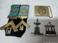 Photo showing all items in the lot, including ribbon pins, belt buckle, and two small monument pins.