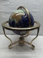 Front angled view of the globe on brass tripod stand showing continents and ocean decoration.