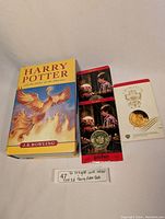 Three sealed Harry Potter collectible coins displayed next to a 1st Canadian edition hardcover of Harry Potter and the Order of the Phoenix.