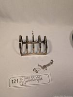 Photo displaying the sterling silver toast rack and the broken silver necklace chain on a fabric surface, with label showing weight and origin.