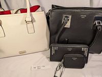 Photo shows two Guess purses (black) and one white Aldo purse side by side along with a small Guess wallet in front.