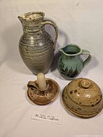 Four pottery items: two pitchers, butter dish with lid, and candle holder with candle seen from front and side angles on white background