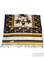 Front view of woven wool Mexican blanket showing central bird and floral design in brown, yellow, orange, black and white colors with fringed edges.