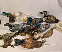 Photo showing front-facing views of 13 duck decoys and figurines arranged on a white surface, capturing color, size, and detail diversity.