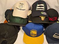 Photo of nine assorted baseball caps and hats arranged in a pile showing front logos and designs.