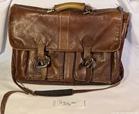 Full front view of the brown leather Hidesign briefcase showing two buckle-closure front pockets and shoulder strap.