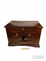 Large wooden jewelry box closed with lock tassel key on front and polished dark wood finish